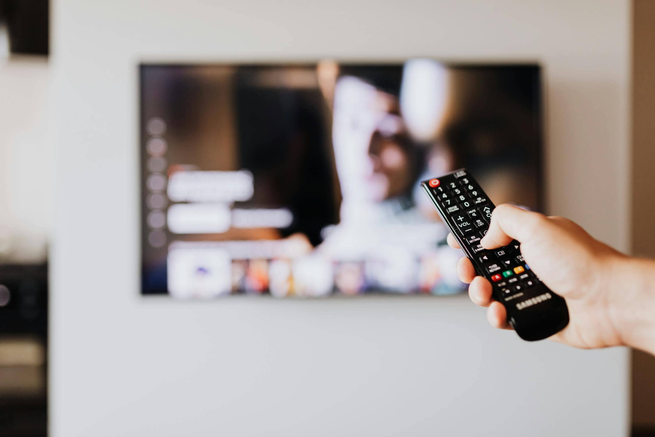 Person holding TV remote control watching streaming series adaptations